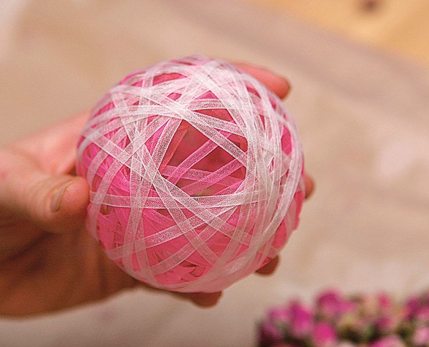 Pembe katmanın üzerine beyaz yarı saydam kurdele sarılmış top elde tutuluyor