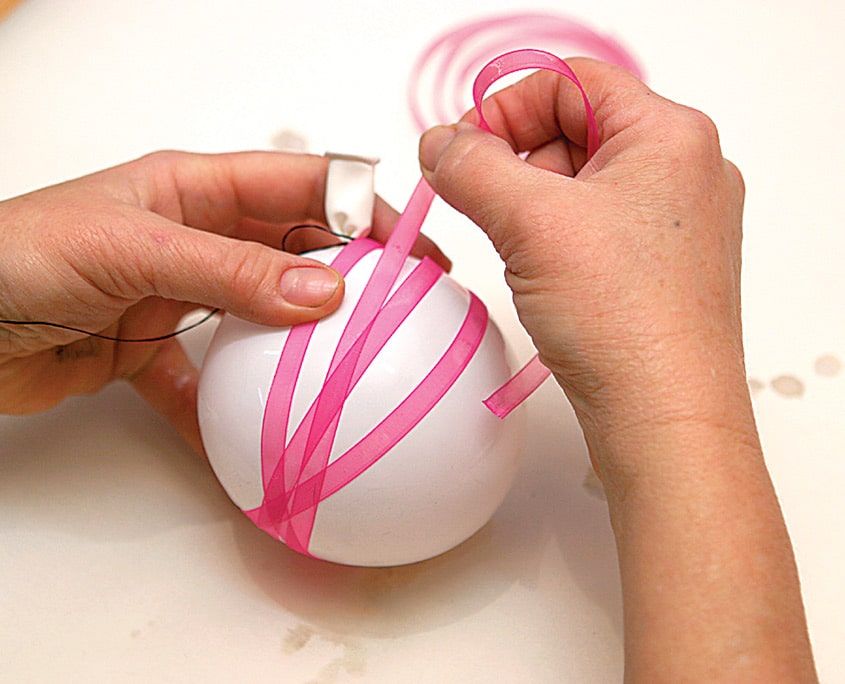 Pembe ipek kurdele beyaz balonun çevresine çapraz şeritler halinde sarılıyor