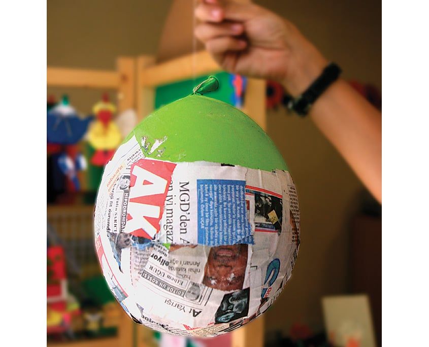 Gazete kağıdıyla kaplanmış yeşil balon kuruması için düğümünden asılı tutuluyor