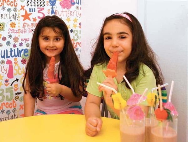 Loli buz: masada ev yapımı meyveli loli buzları tutan iki çocuk, önlerinde pipetli bardaklar