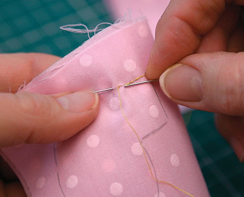 Puantiyeli pembe kumaştan küçük parçalar iğne ve iplikle çizgi boyunca dikiliyor