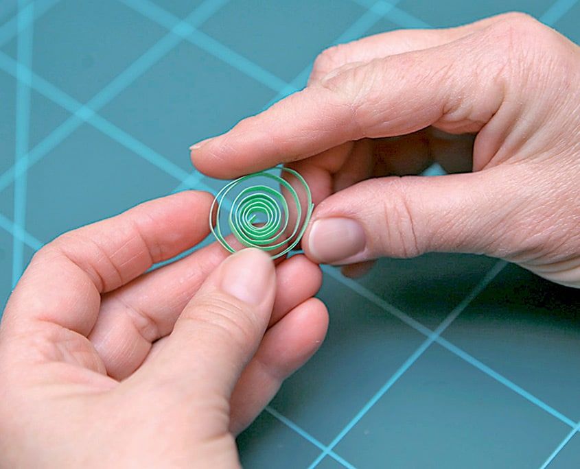 Açık yeşil gevşek quilling spirali parmaklar arasında tutuluyor