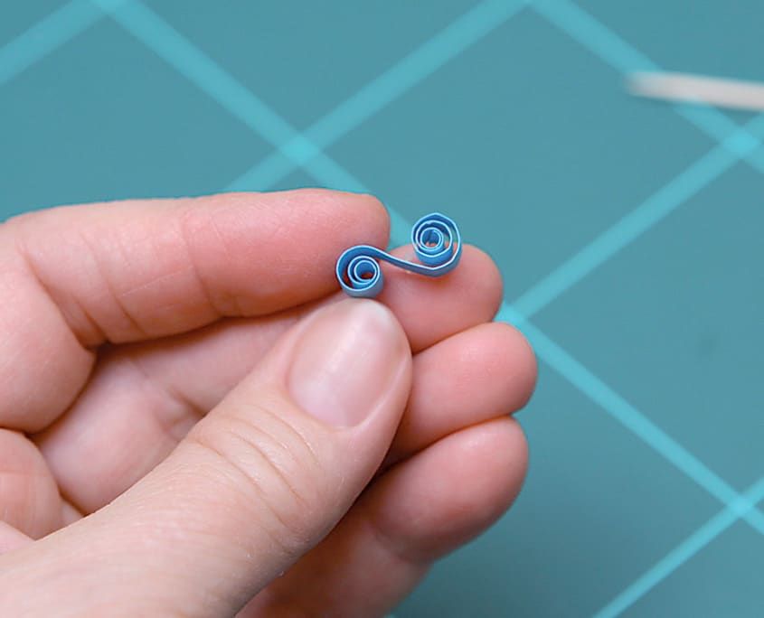İki ucu içe kıvrılmış mavi quilling süs parçası parmak ucunda