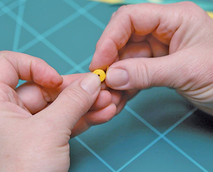 Parmak uçları arasında sıkı sarılmış küçük sarı quilling rulosu