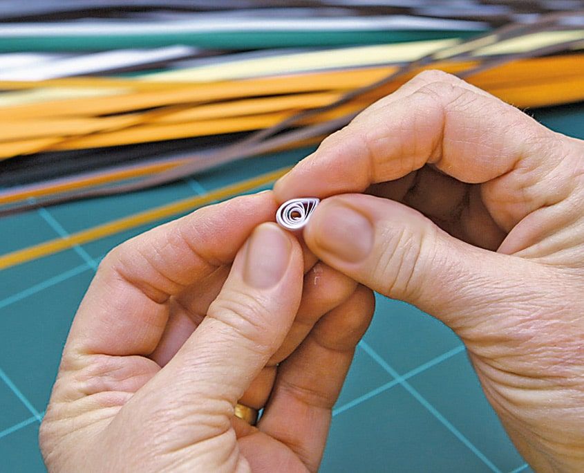 Çubuktan çıkarılan beyaz quilling rulosu parmaklar arasında gevşetilerek açılıyor