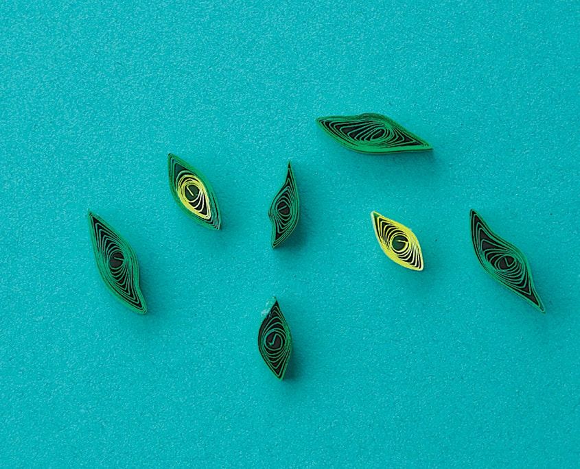 Turkuaz zeminde dağınık duran yeşil tonlarda sivri uçlu küçük quilling yapraklar