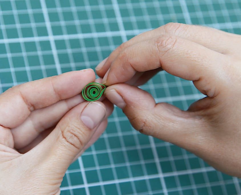 Parmaklar arasında gevşetilmiş koyu yeşil quilling spirali, yaprak için hazırlanıyor