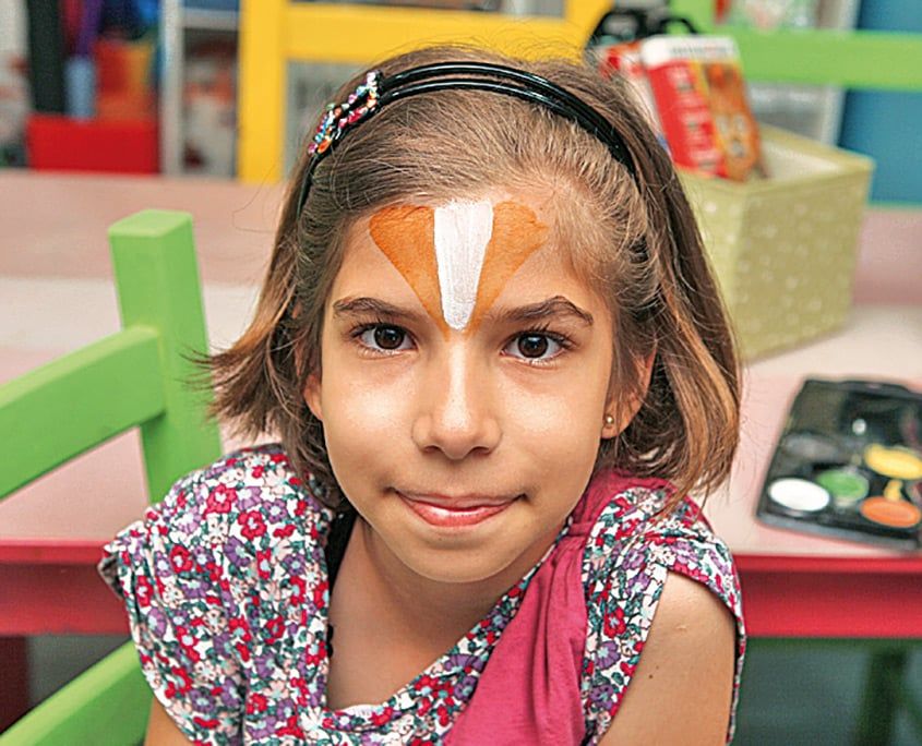Yüz boyamanın ilk adımı: alna beyaz dikey şerit ve iki yanına turuncu boya sürülmüş