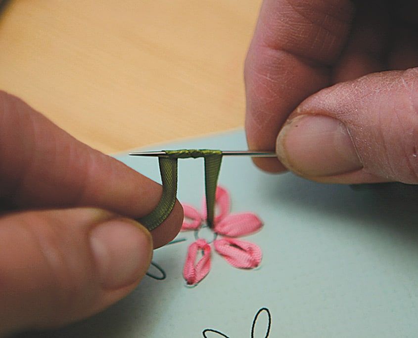 Pembe yapraklı çiçeğin sapı için yeşil kurdele iğneyle karta dikiliyor