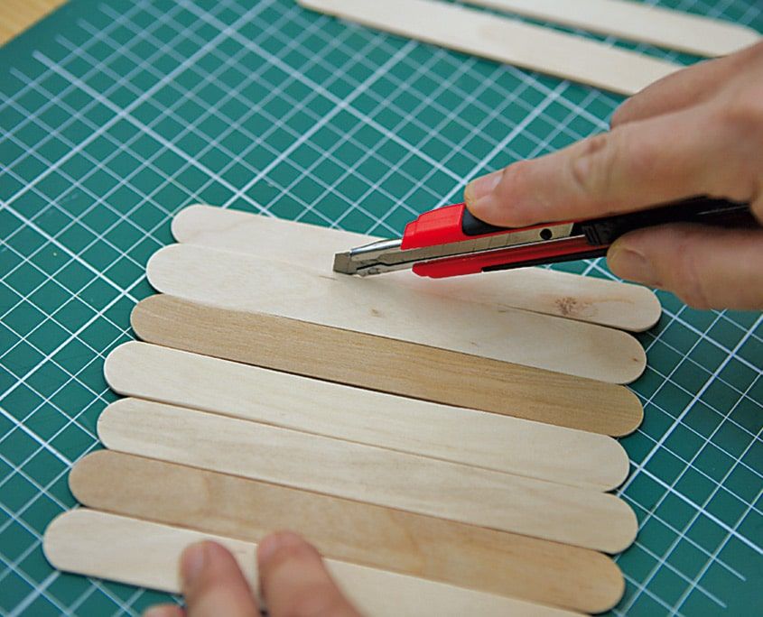 Yan yana dizilmiş dondurma çubuklarının maket bıçağıyla ölçüye göre hizalanması