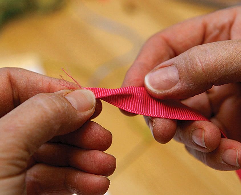 Önlük bağcığı olacak pembe grogren kurdelenin ucu parmaklar arasında katlanıyor