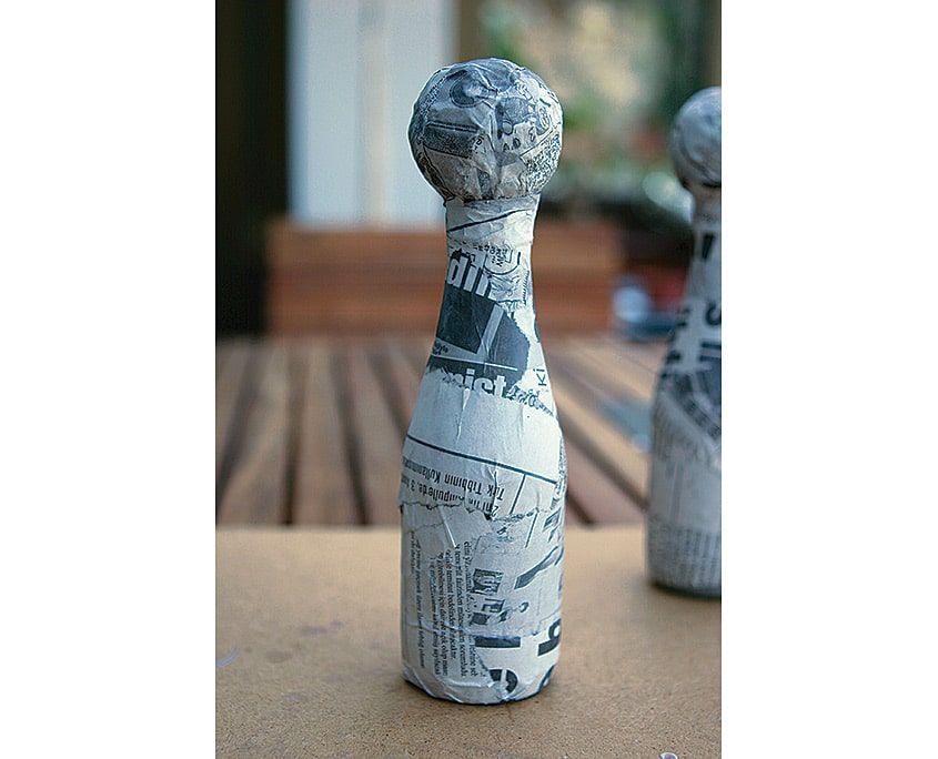 Gazete kağıdıyla kaplanmış tek şişe palyaço gövdesinin yakından görünümü, yazılar seçiliyor