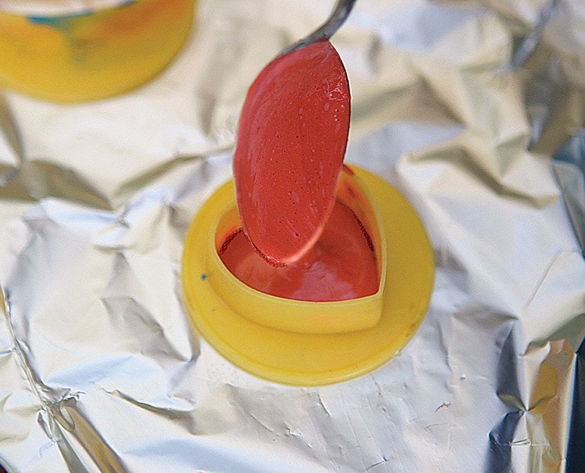 Kaşıkla erimiş kırmızı pastel boya, alüminyum folyo üzerindeki sarı plastik kalıba dökülüyor