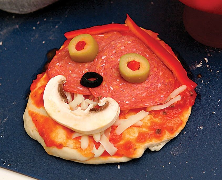 Yakın plan pişmiş mini pizza: zeytin gözler, mantar ağız, salam yüz ve kırmızı biber saçlar