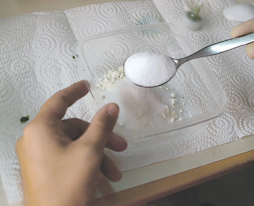 Kabaran boya için plastik kaptaki una kaşıkla tuz ekleniyor, kağıt havlu serili masada