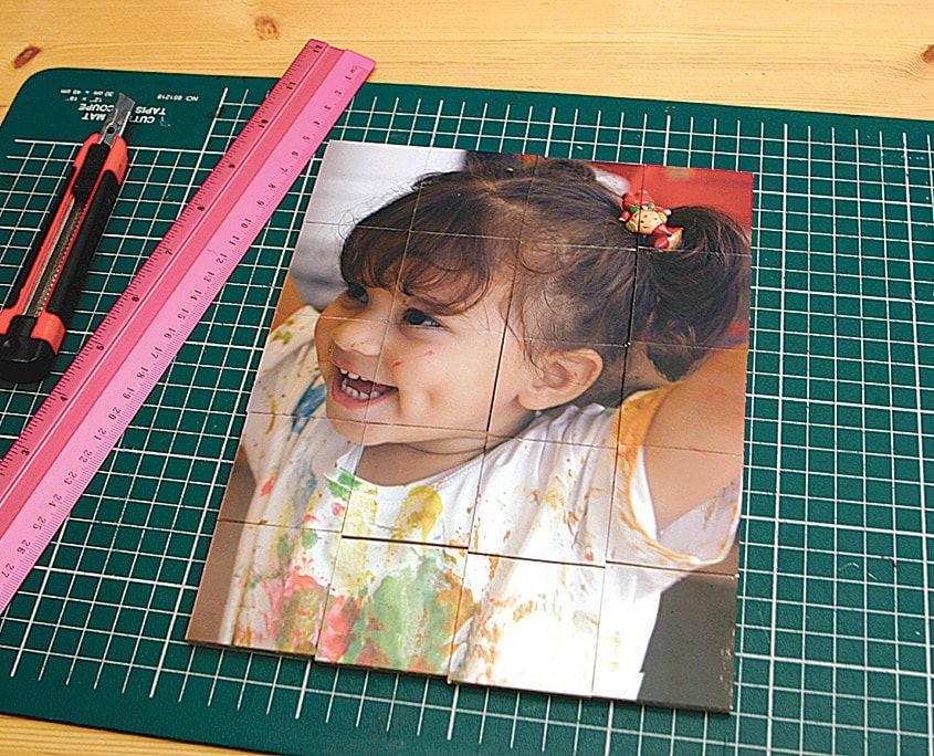 Kesim altlığında kartona yapıştırılmış çocuk fotoğrafı, yanında pembe cetvel ve maket bıçağı