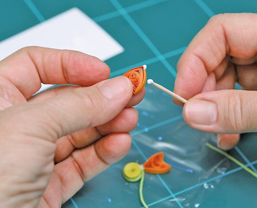 Turuncu quilling yaprağının kenarına kürdanla tutkal sürülüyor, naylonda sarı göbek ve ip