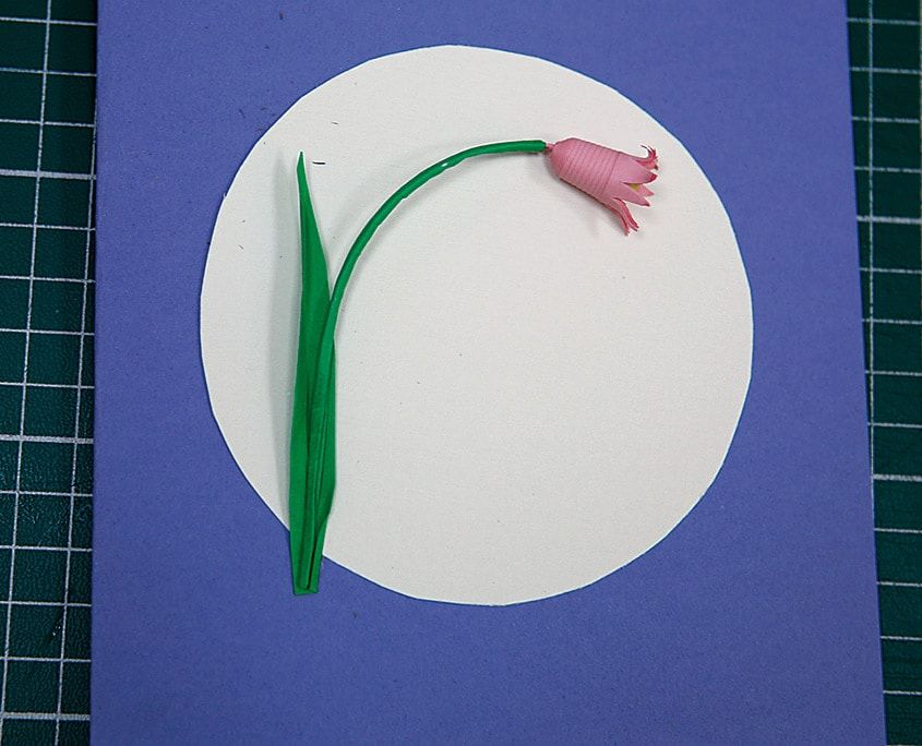 Lacivert karttaki beyaz daireye yeşil kıvrık saplı ve yapraklı tek pembe quilling çan çiçeği yapıştırılmış