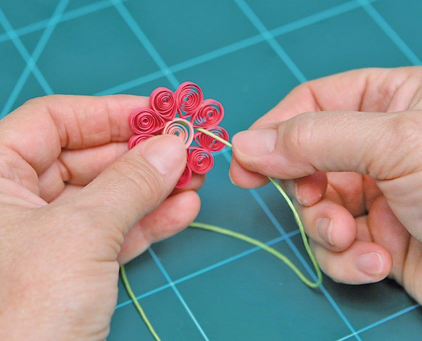 Pembe sarmal quilling çiçeğin ortasındaki boşluktan açık yeşil kolye ipi geçiriliyor
