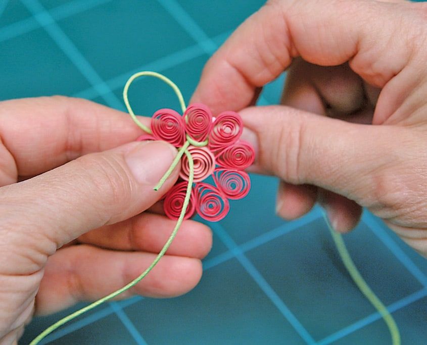 Pembe quilling çiçeğin üstünde açık yeşil ipten düğümlü askı ilmeği sıkıştırılıyor