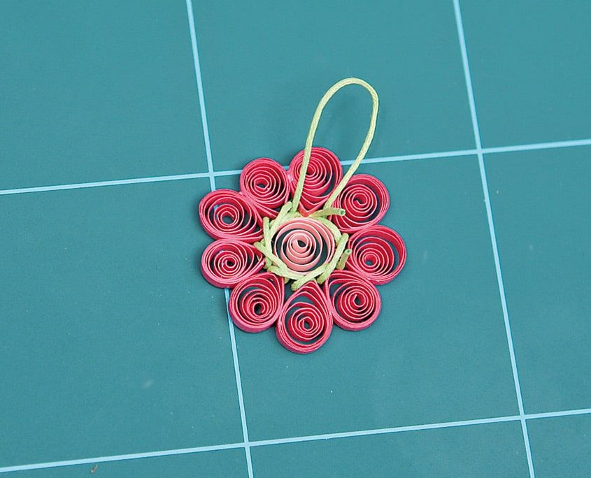 Tamamlanmış pembe quilling çiçek kolye ucu, ortası açık yeşil ip düğümlü, kesim altlığında