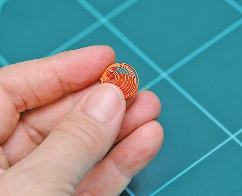 Turuncu kağıt şerit sarılıp bırakılınca açılmış gevşek quilling spirali parmaklar arasında