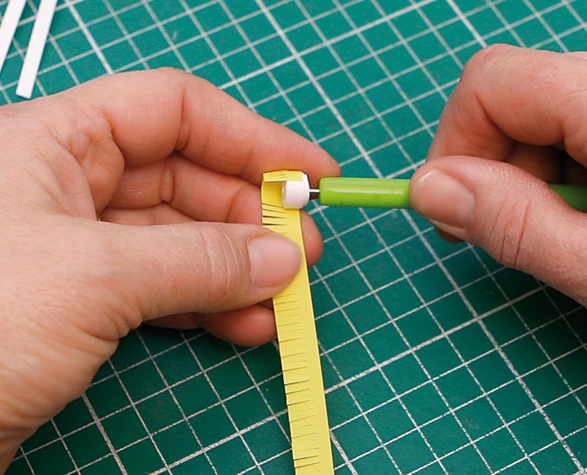 Saçaklı sarı şerit beyaz göbeğin çevresine quilling kalemiyle sarılıyor