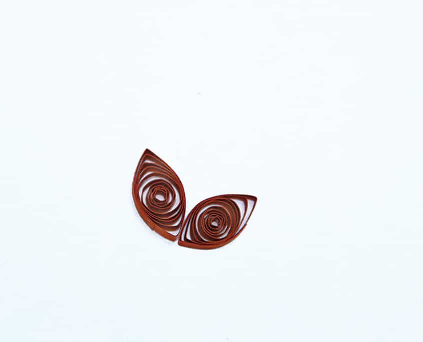 Beyaz zeminde yan yana yapıştırılmış iki koyu kırmızı damla quilling, lale tacının iki yanı