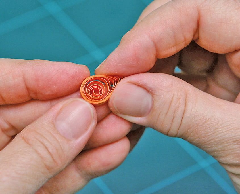 Gevşek turuncu quilling spirali iki parmakla sıkıştırılarak biçim veriliyor
