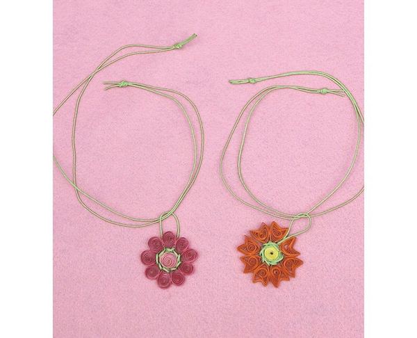 Quilling çiçek kolye: pembe zemin üstünde ince iple asılı mor ve turuncu kağıt dolama çiçek kolyeler