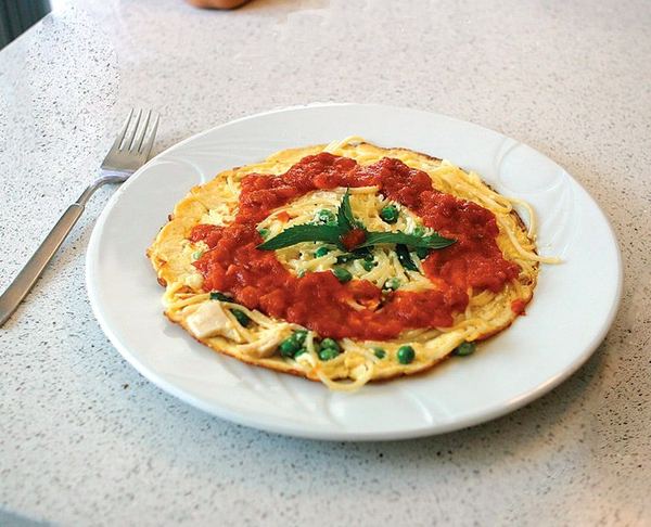 Makarnalı pancake: beyaz tabakta bezelyeli yumurtalı makarna, üzerinde domates sosu ve fesleğen yaprakları
