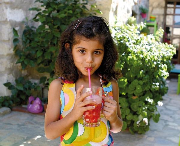 Ev yapımı çilekli limonatayı bahçede pipetle içen bir çocuk, elinde kırmızı içecek dolu bardak