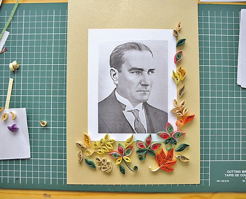 Atatürk portresinin kenarlarına dizilmiş sarı, turuncu ve yeşil quilling çiçek ve yapraklar