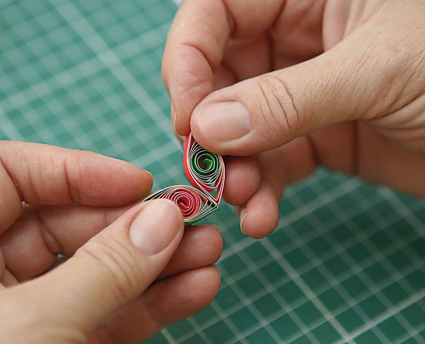 İki ucu sıkıştırılmış kırmızı-yeşil yaprak biçimli quilling parçaları parmaklar arasında