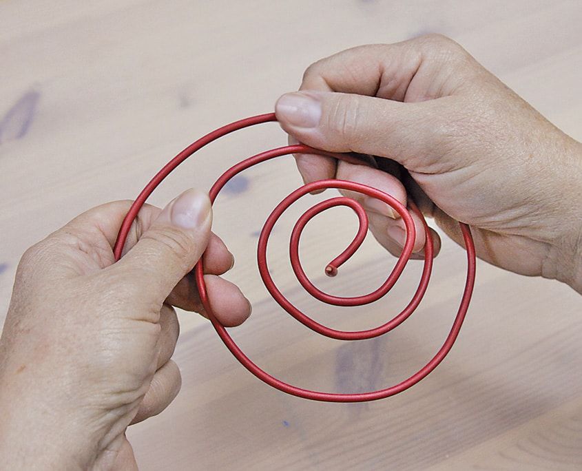 Kırmızı kaplı tel eller arasında büyükten küçüğe iç içe spiral biçiminde kıvrılmış