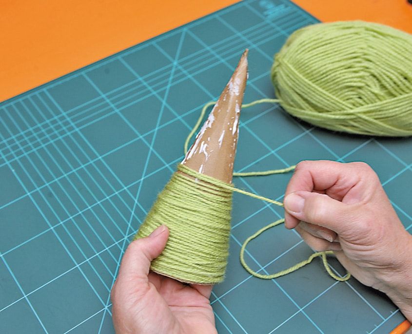 Karton koninin çevresine alttan başlayarak açık yeşil yün iplik sarılıyor