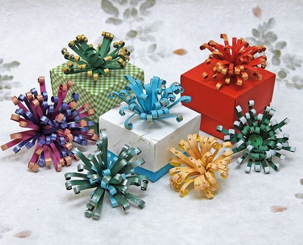 Quilling ile paket süsleri: hediye kutularının üstünde mor, mavi, yeşil ve sarı püsküllü kağıt fiyonklar