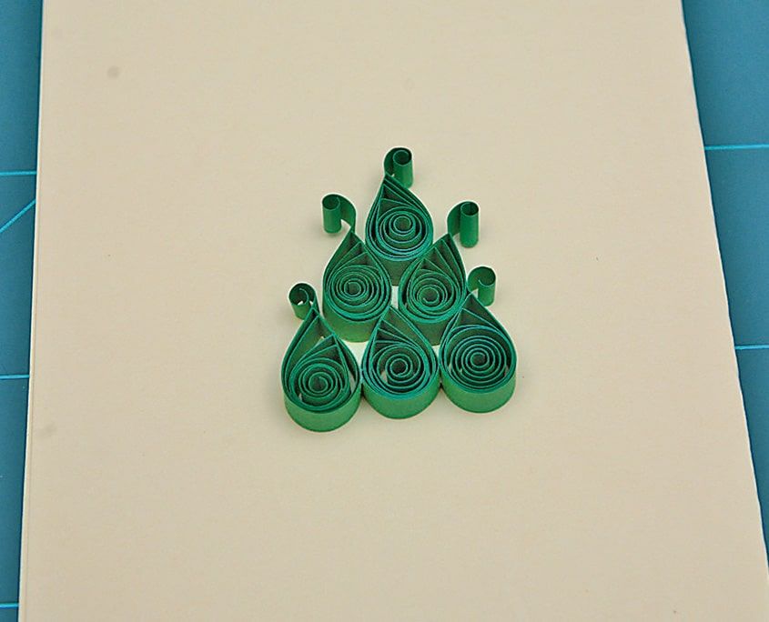 Krem karton üzerinde üçgen biçiminde birleştirilmiş yeşil quilling damlalardan ağaç gövdesi