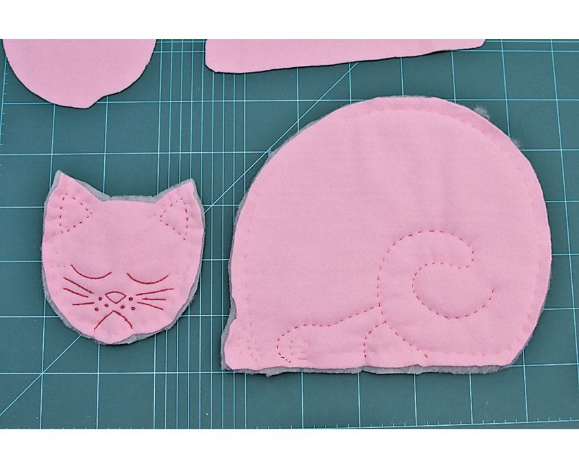 Yüzü nakışlanmış pembe kedi başı ve kuyruk sarmalı dikiş çizgisiyle işlenmiş gövde parçası