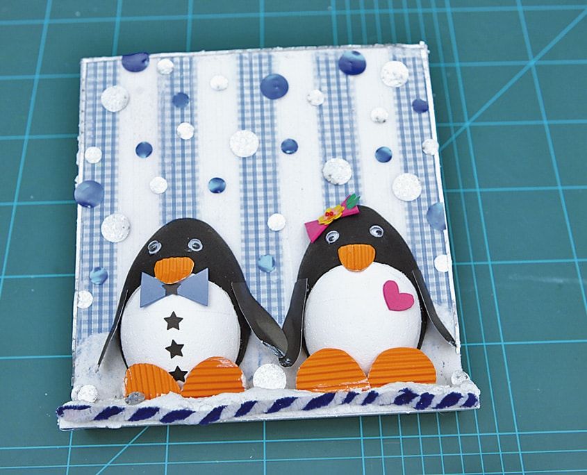 Tamamlanmış Penguen Kardeşler panosu: pullar ve boncuklarla süslü fon, alt kenarda burgulu kordon