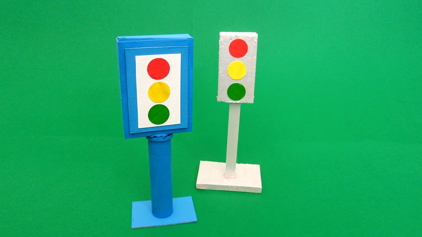 Mavi ve beyaz kartondan iki trafik lambası, kırmızı, sarı, yeşil ışıklarıyla yeşil zeminde