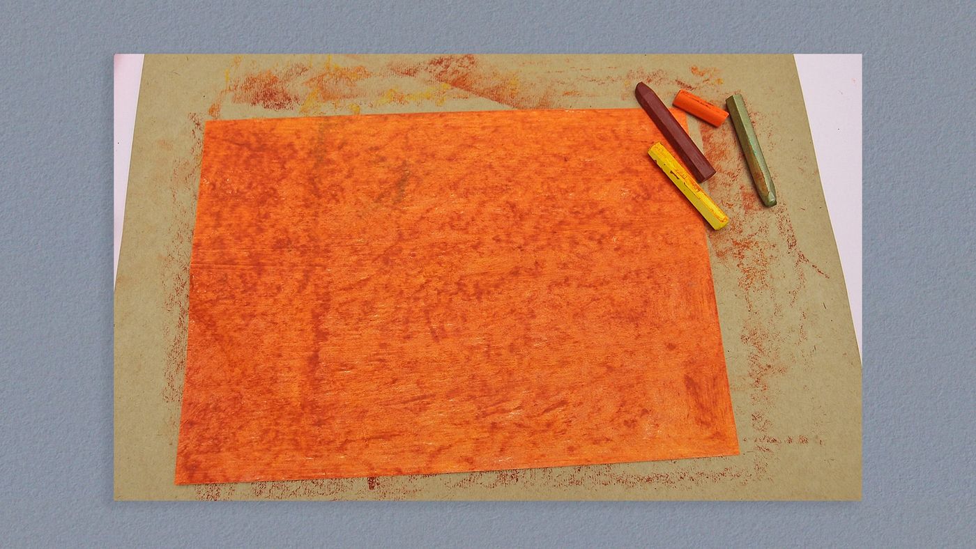 Kahverengi karton üzerinde turuncu pastel boyayla tamamen boyanmış kağıt, yanında pastel boyalar