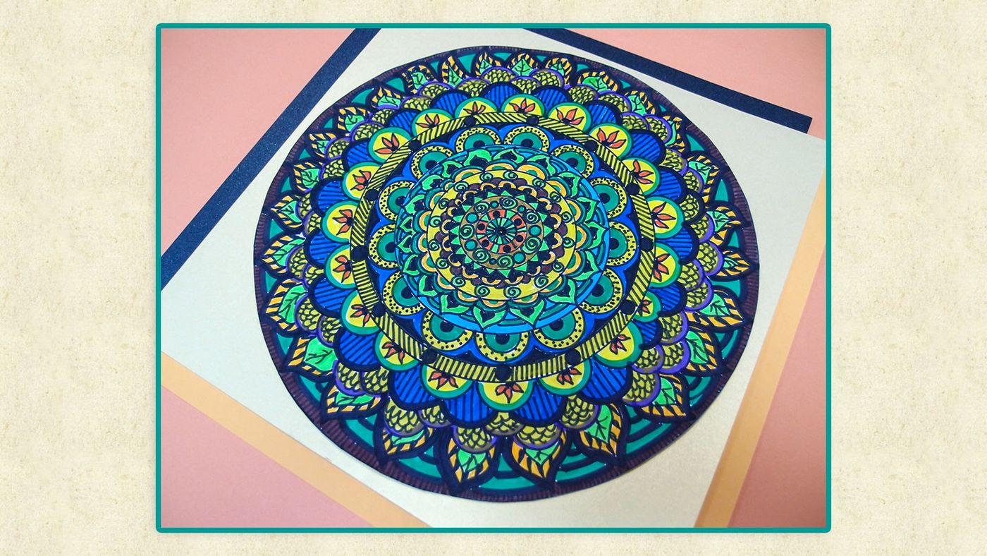 Mandala III bitmiş çalışma: renkli mandala turkuaz çerçeveyle krem kağıt üzerinde, eğik açıdan