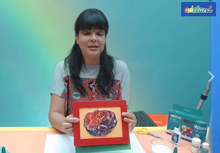 Canlı atölye yayınından kare: eğitmen kırmızı çerçeveli renkli ebru çalışmasını gösteriyor