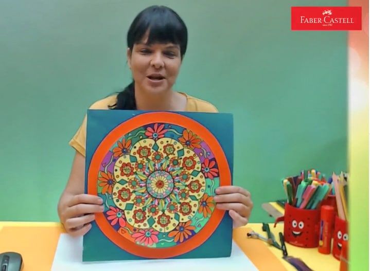 Mandala atölyesi II yayınından kare: eğitmen turuncu çerçeveli çiçekli mandalayı gösteriyor
