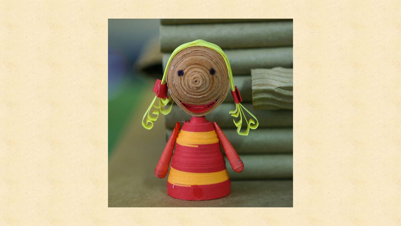 Kahverengi sarmal yüzlü, kırmızı-sarı çizgili elbiseli ve kırmızı tokalı quilling kız kukla