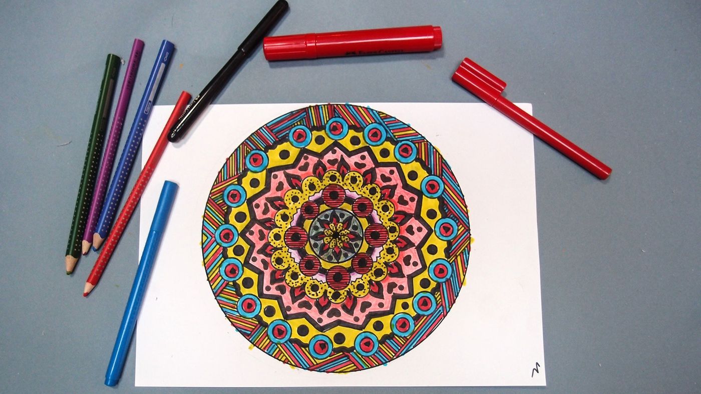 Sarı, pembe, mavi ve kırmızı keçeli kalemle renklendirilmiş mandala, çevresinde kalemler