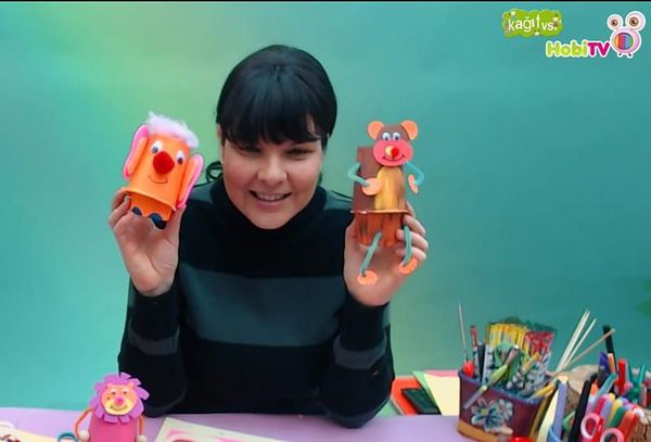 Bardak Hayvanlar video karesi: eğitmen kağıt bardaktan yapılmış iki hayvan kuklasını elinde gösteriyor