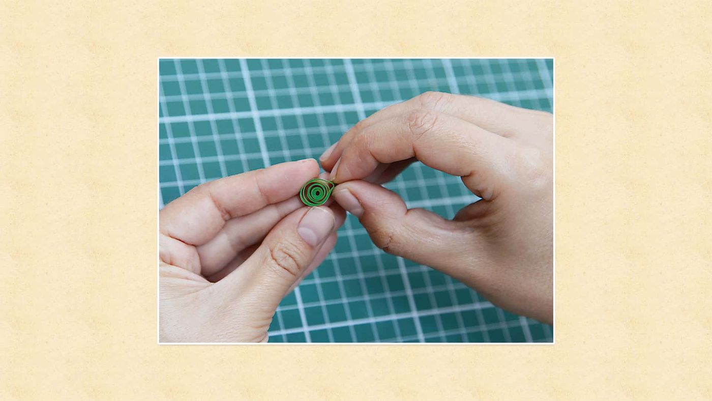Sıkı sarılmış yeşil quilling rulosu iki parmak arasında bastırılarak şekil veriliyor