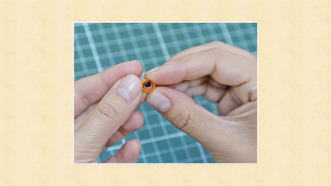 Parmaklar arasında siyah merkezli turuncu quilling rulosu, baykuş gözü olarak kullanılacak